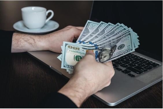 Person counting US dollar bills in front of a laptop, symbolizing online earning or making money online in 2024